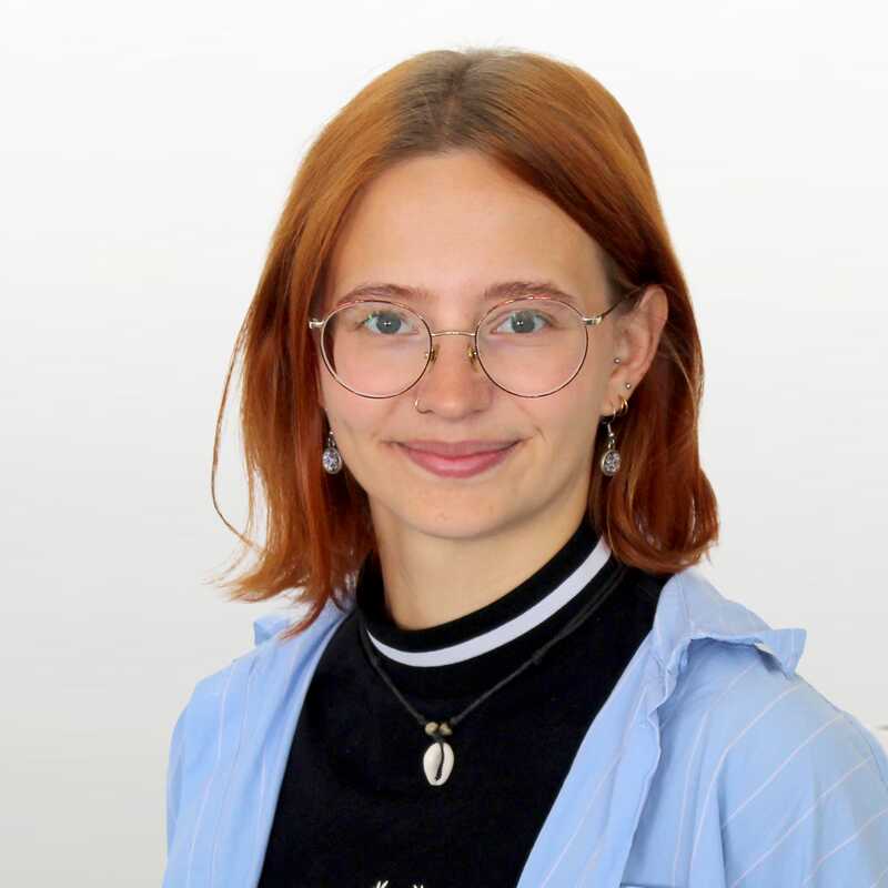 Junge Frau mit schulterlangen Haaren und einer Brille lächelt freundlich in die Kamera.