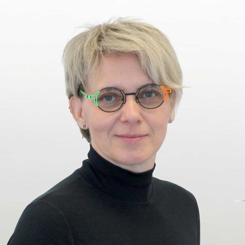 Portätbild einer Frau mit hellen Haaren und einem dunklem Pullover. Dazu trägt Sie eine getönte Brille mit farbigen Akzenten.