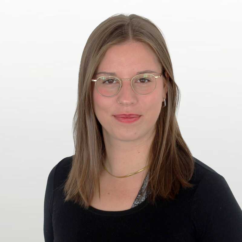 Junge Frau mit Brille und offenen, dunklen Haaren lächelt leicht in die Kamera