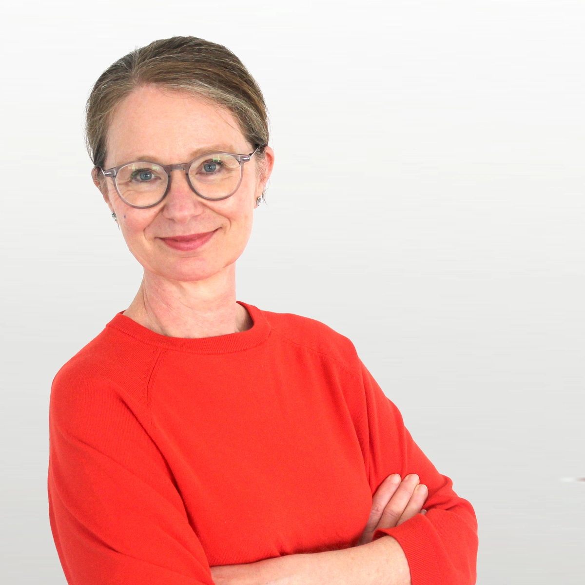 Frau mit rotem Pullover, Brille und zusammengebundenen Haaren lächelt in die Kamera